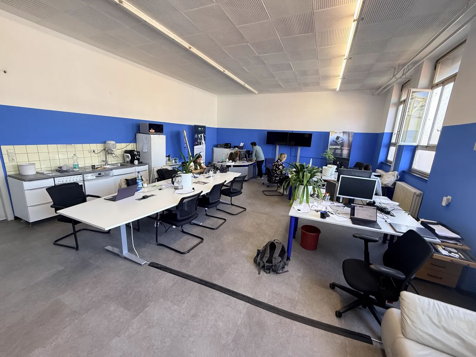 Open-plan office with a long desk row, kitchenette and blue wall framing