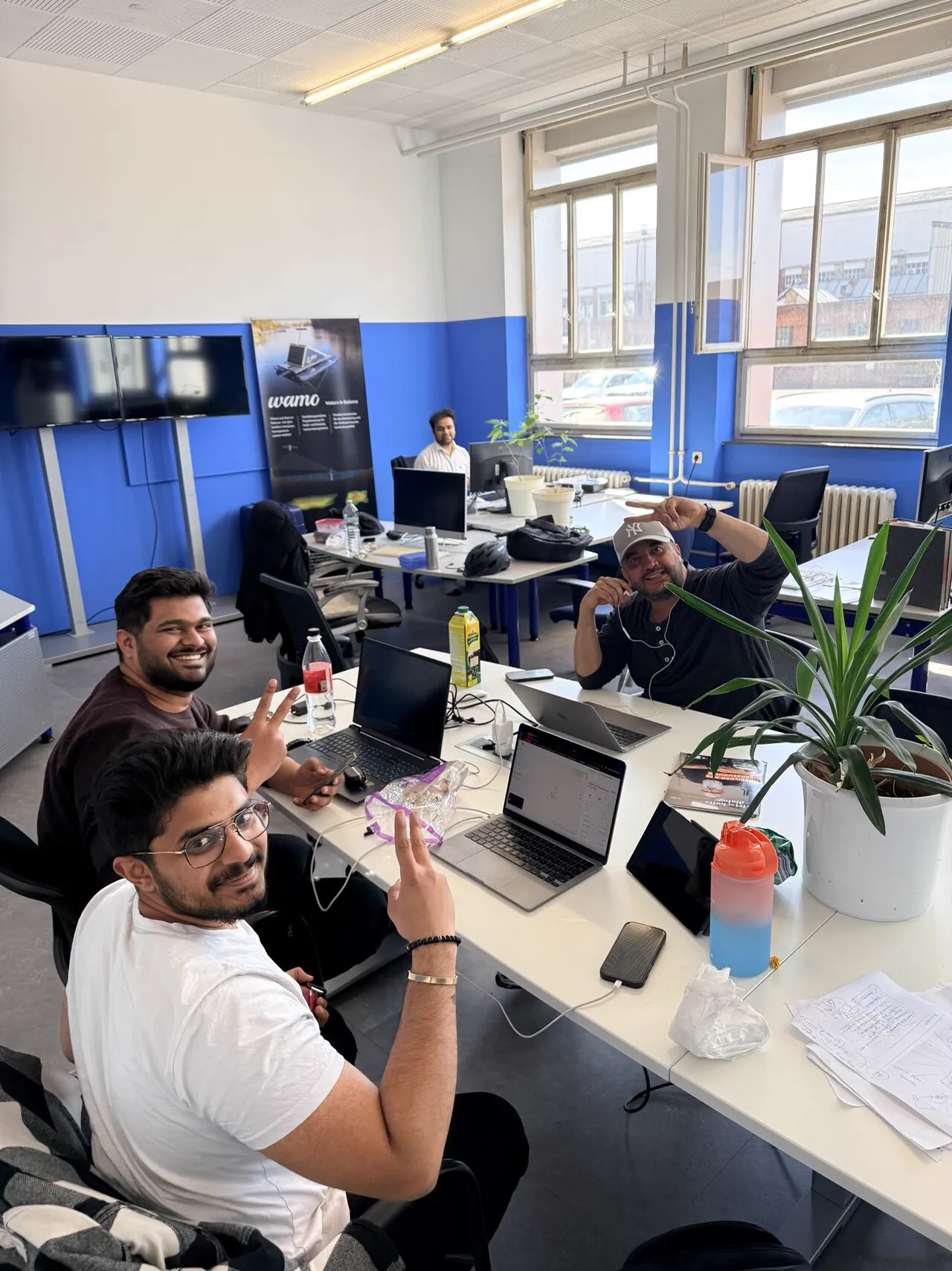 Three colleagues at a shared desk with laptops and plants