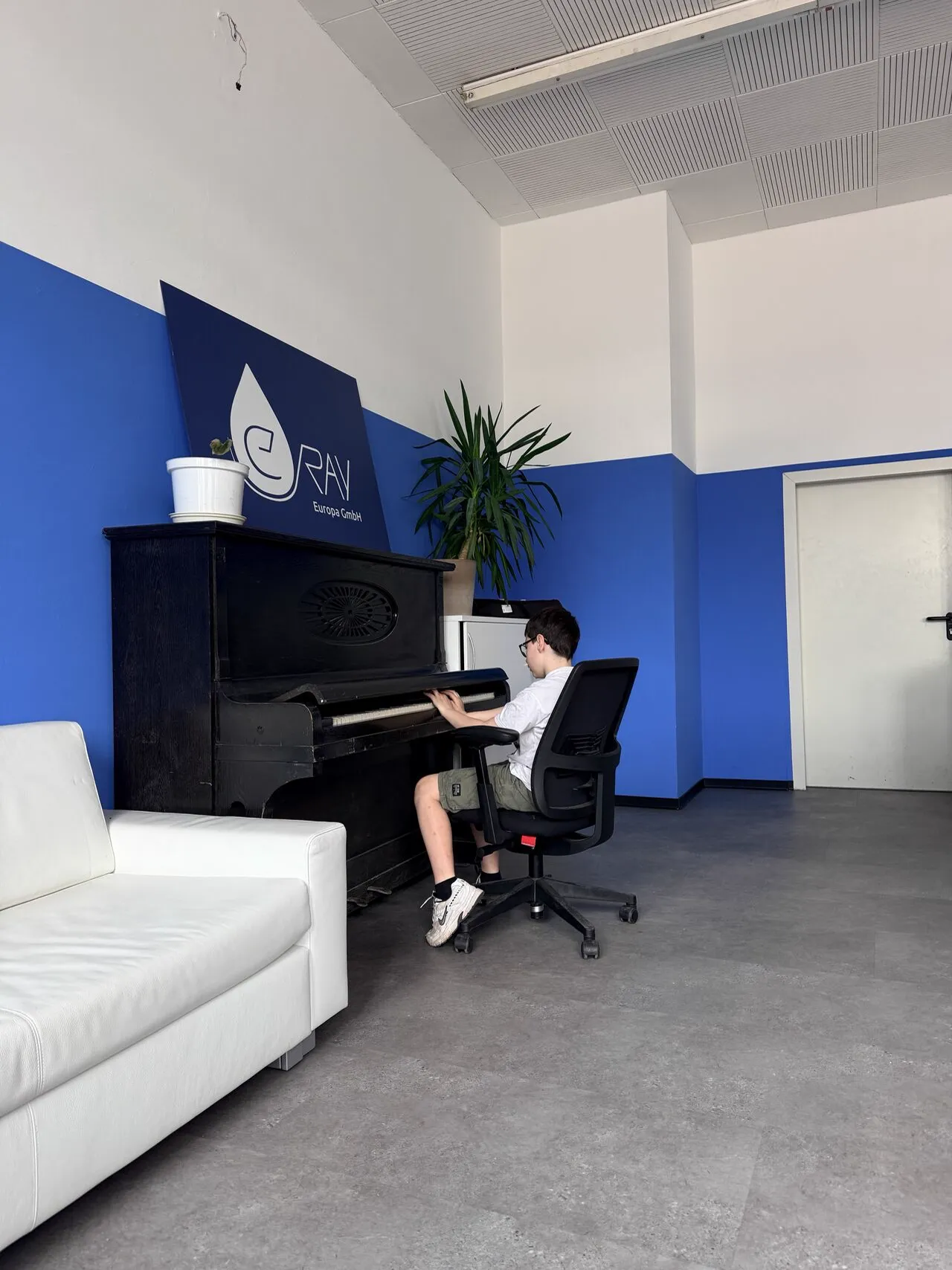 Colleague playing the old piano in front of the blue wall with eRay logo