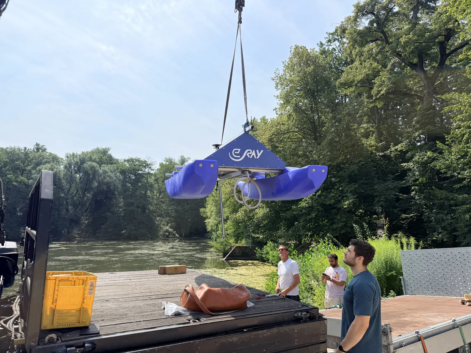 A crane lowers the WAMO station into the Backhausteich while the team stands on the bank