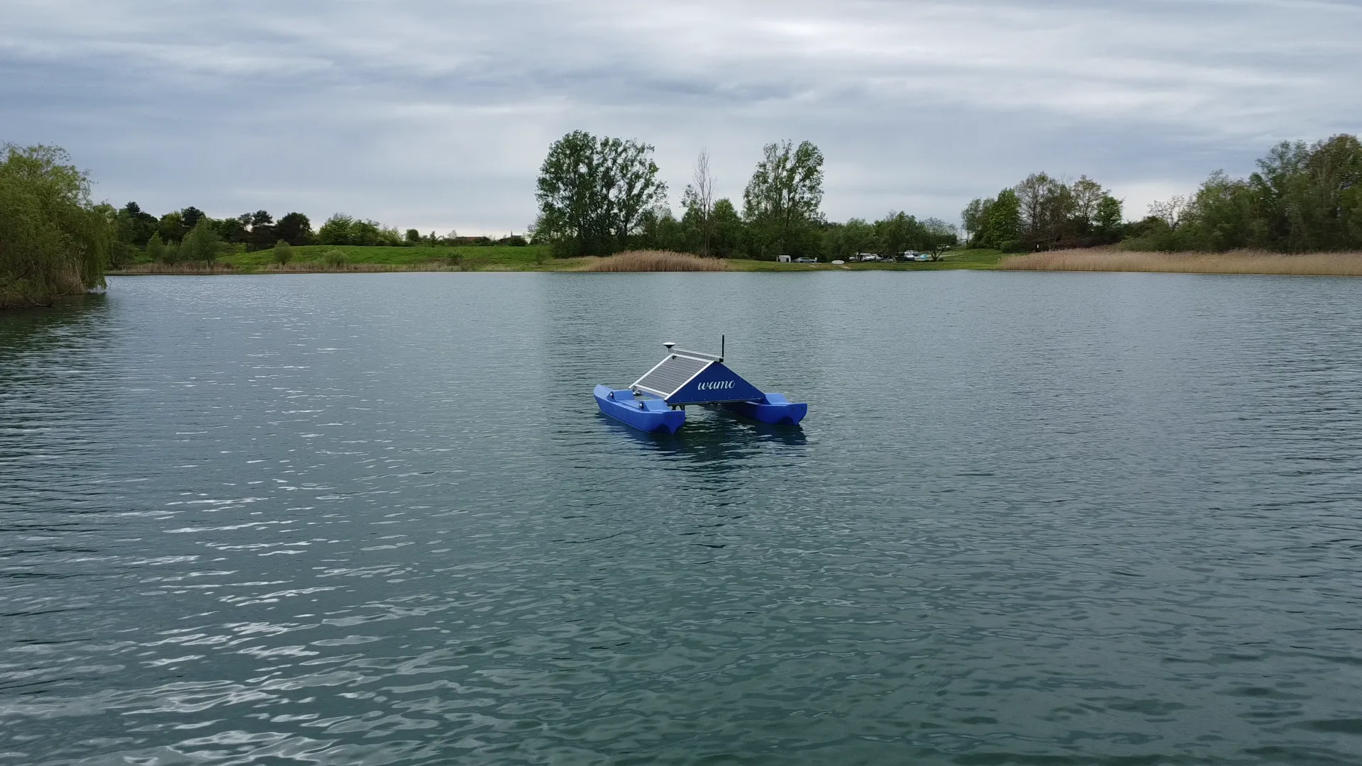 Blue WAMO monitoring station with solar module on a lake, wooded shoreline in the background